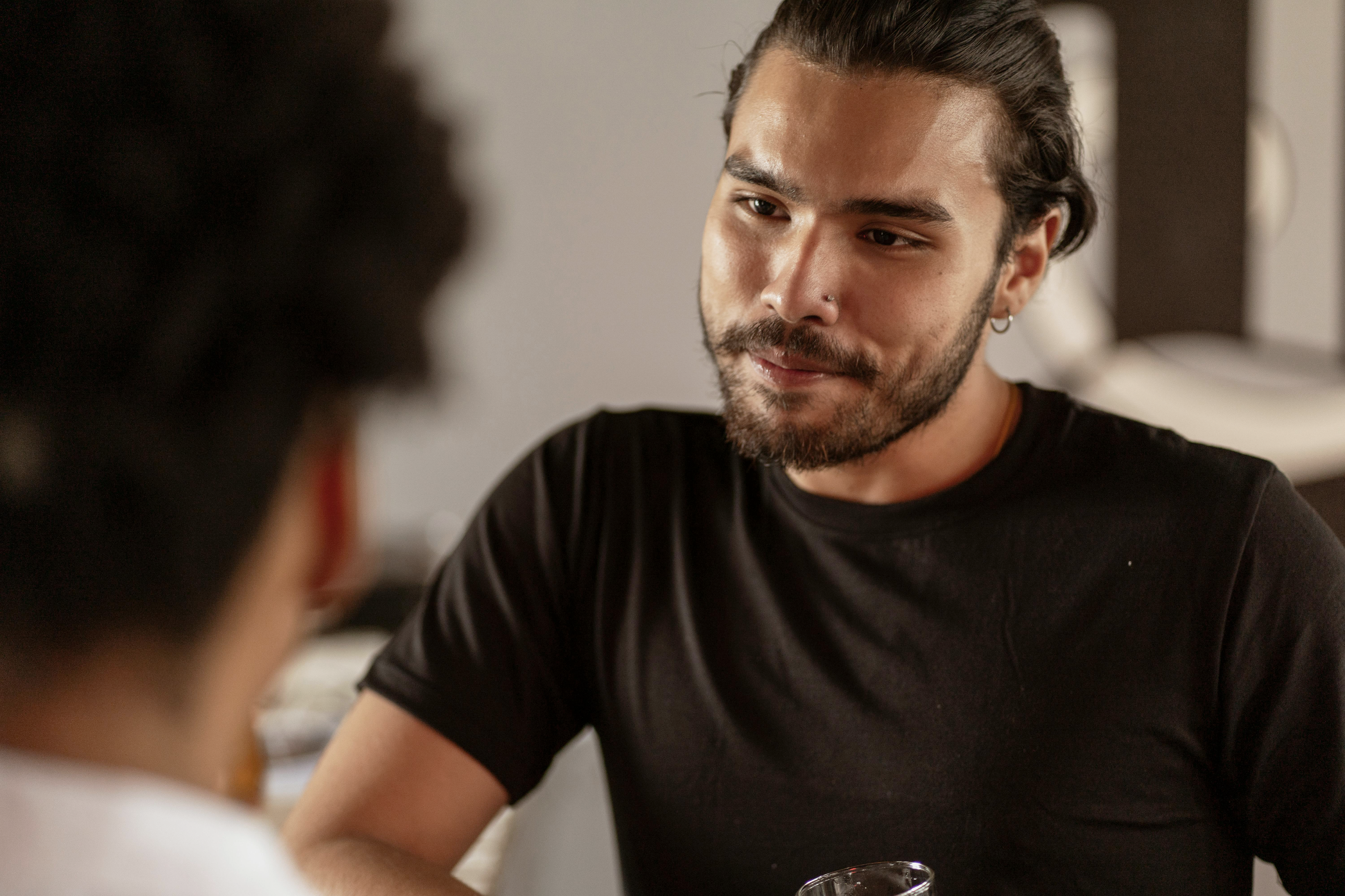 Two Latine men in conversation, with one intently listening in an indoor setting